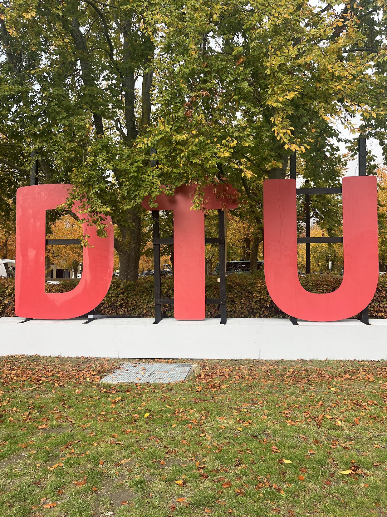 The red DTU letters on campus in Kongens Lyngby, autumn leaves on the ground