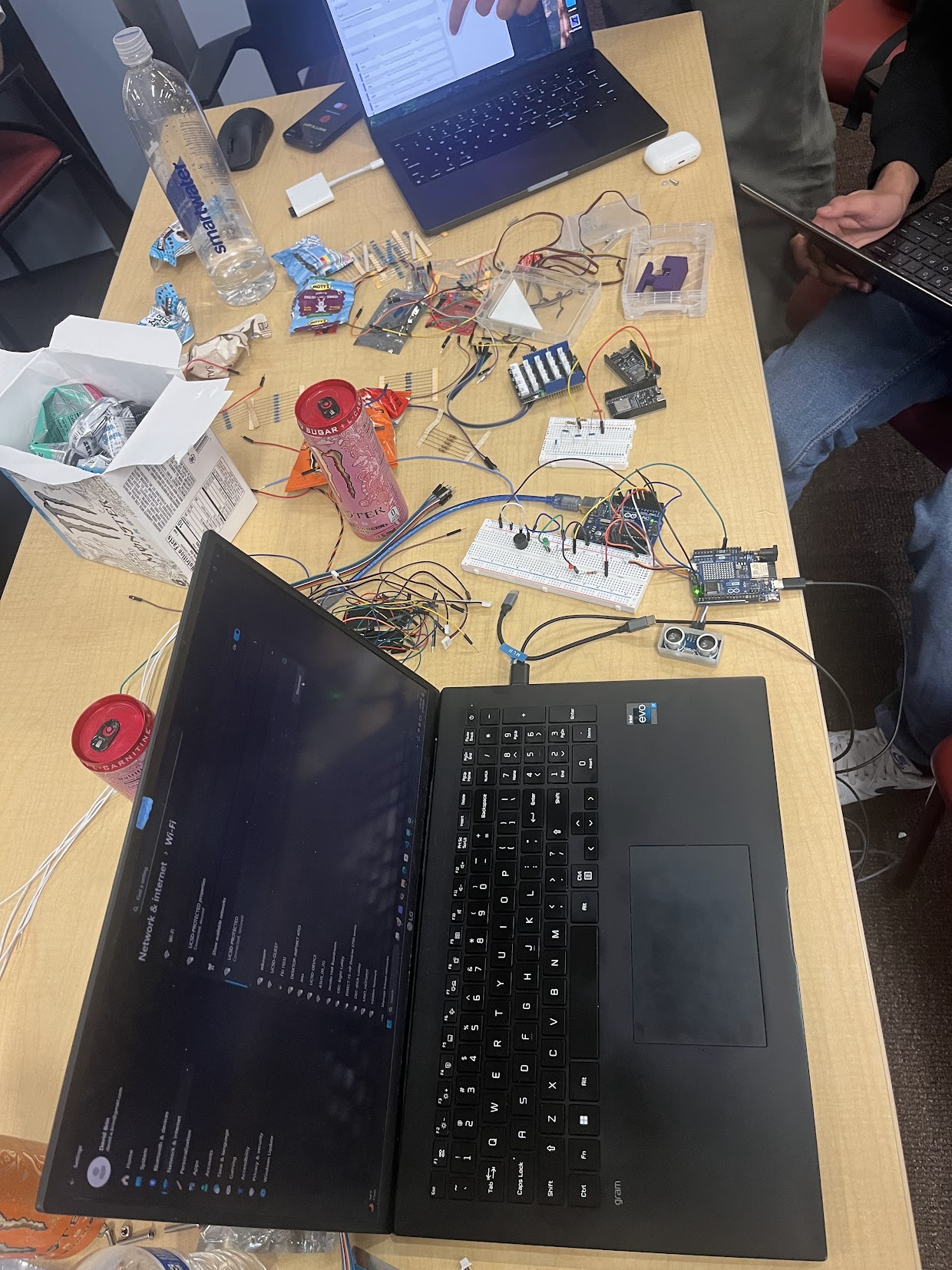 A HardHacks workbench mid-build: breadboards, an Arduino, jump wires, sensors, and two laptops